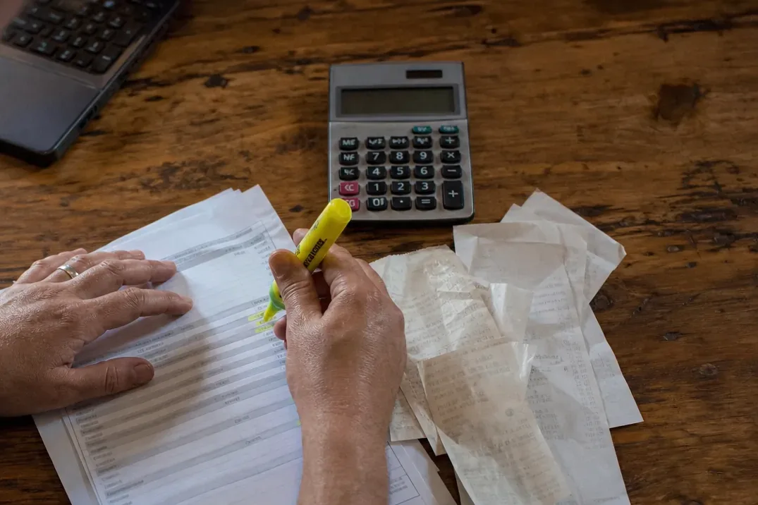 Vendor bills and a calculator on a wooden desk while a bill is ticked off