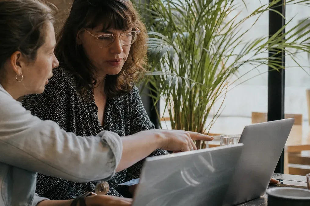 Two bookkeepers comparing subscription costs on their laptops at a shared table