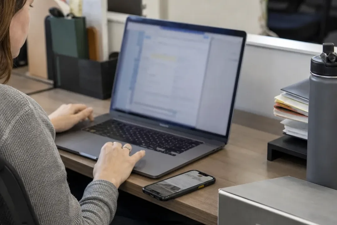 Bookkeeper working through emailed receipts on a laptop with a phone on the desk