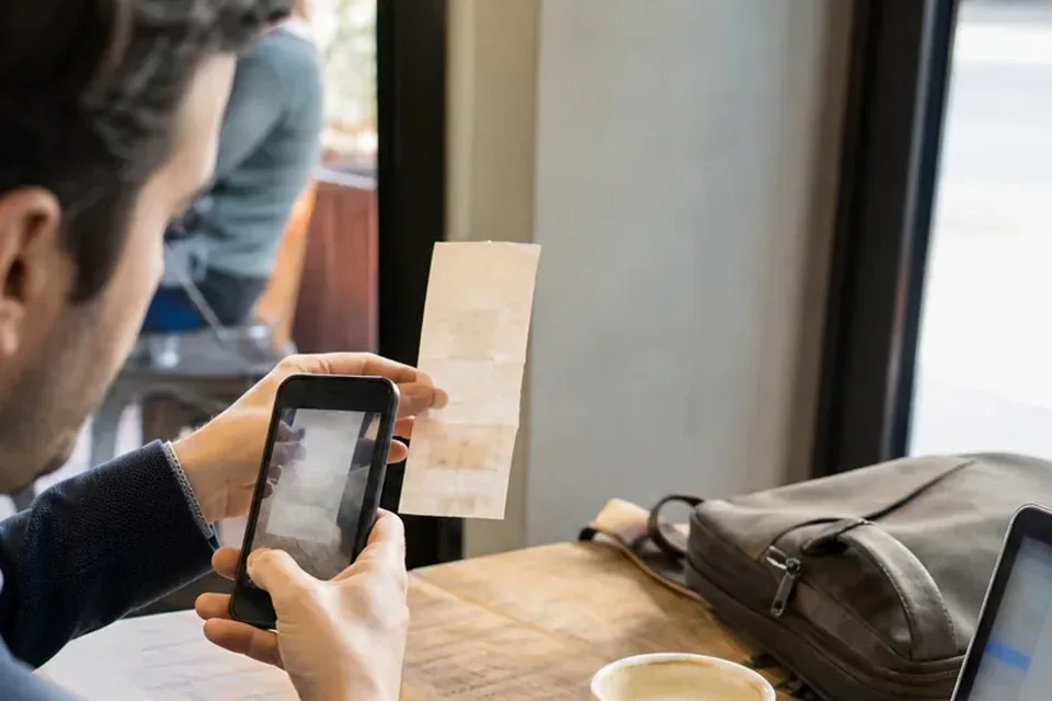 Phone camera framing a paper lunch receipt held up at a cafe table