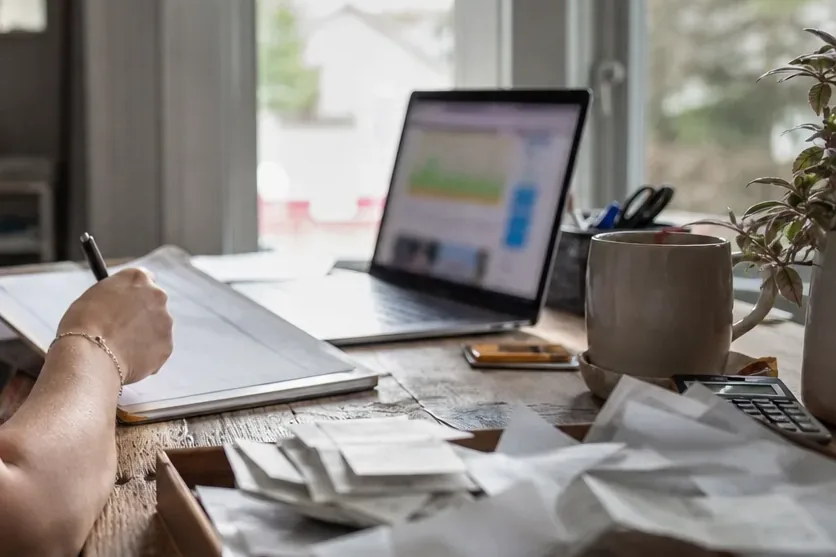 Tray of paper receipts and a calculator next to a laptop on a home office desk